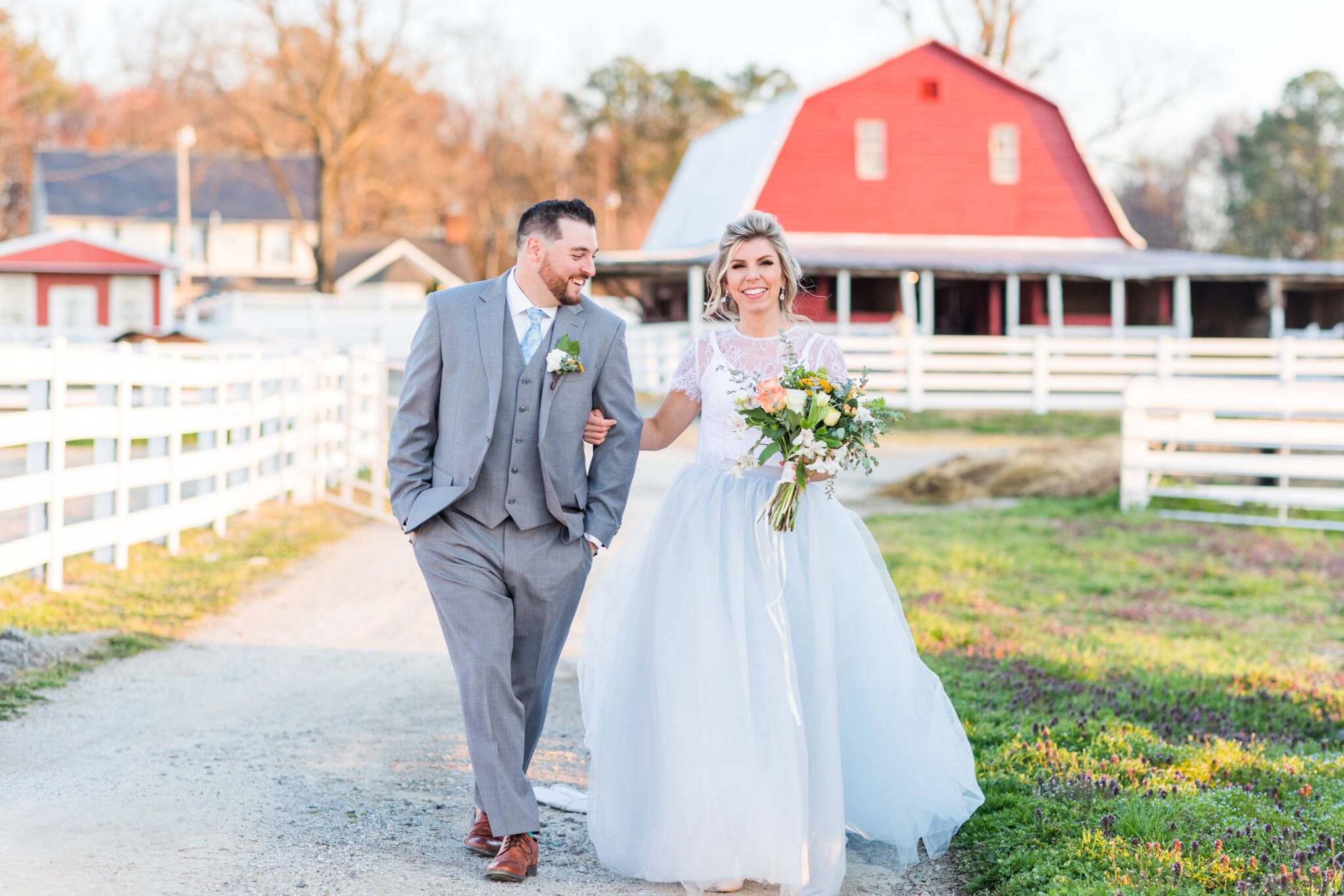 A couple walking beside the white fence and red barn at Sears Farms